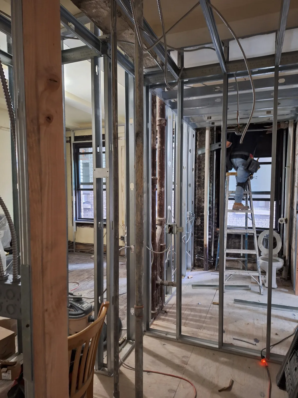 Licensed AE Electric electrician on a ladder running new BX cable through an open ceiling during a NYC house rewire
